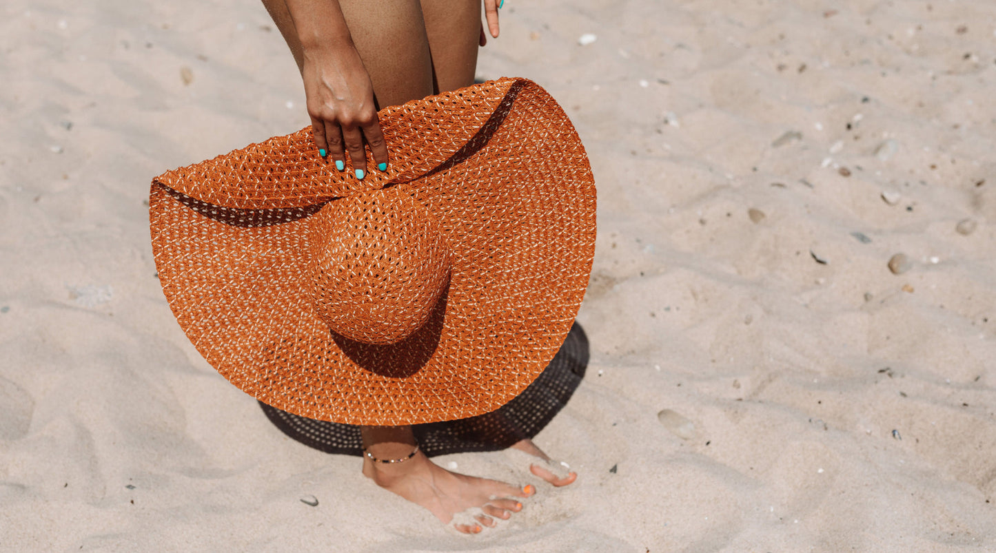 Woman holding a large woven sun hat while walking barefoot on a sandy beach, capturing a warm summer scene with natural sunlight.