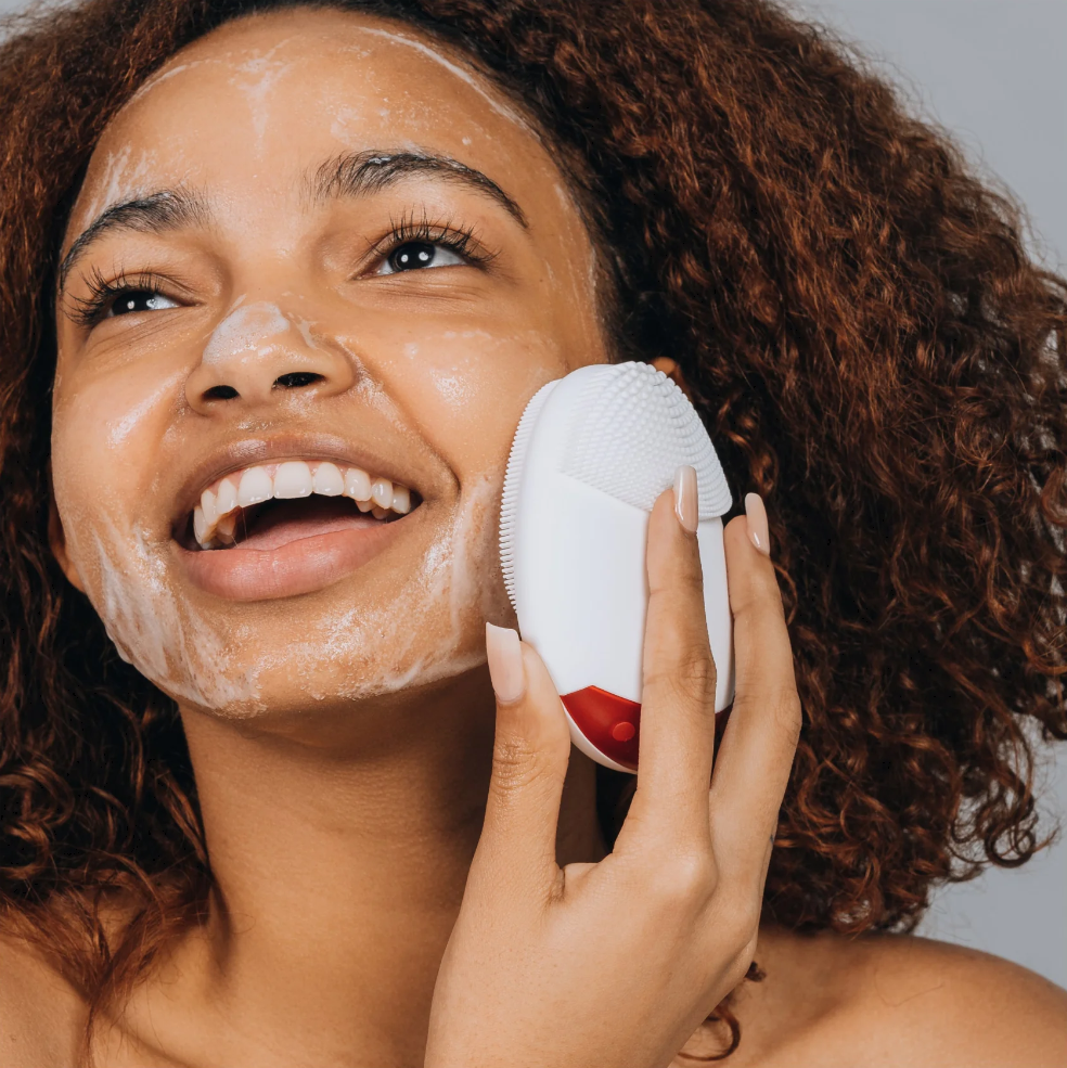 A woman using StimuBrush, a smart facial cleansing brush.